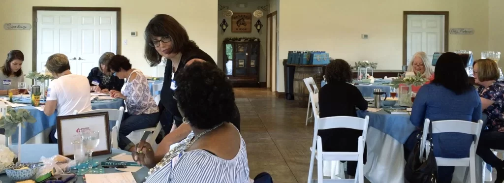 Izolda helping a workshop participant while others work on their creative projects at tables.